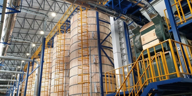 Vnitřní pohled na obilné silo s kovovými nádržemi a žlutým zábradlím.