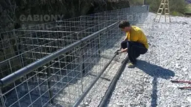 Muž montuje ocelový plot z kbelíků s kamením na skále.