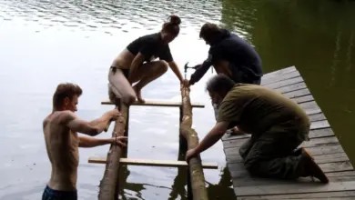 Čtyři lidé staví dřevěný molo na vodě vlastníma rukama.
