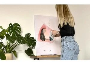 Žena zavírá obrázek na zeď pomocí lepicí pásky.