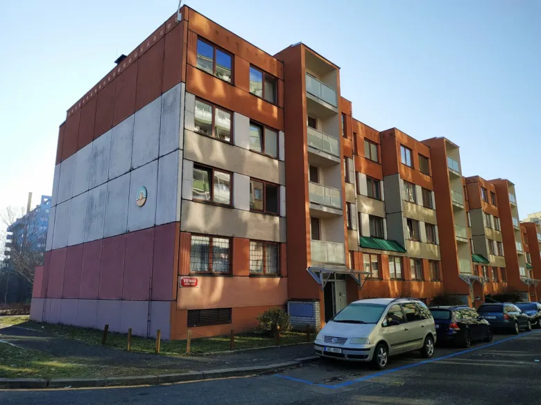 Moderní panelový dům s barevnou fasádou na pozadí parkoviště.