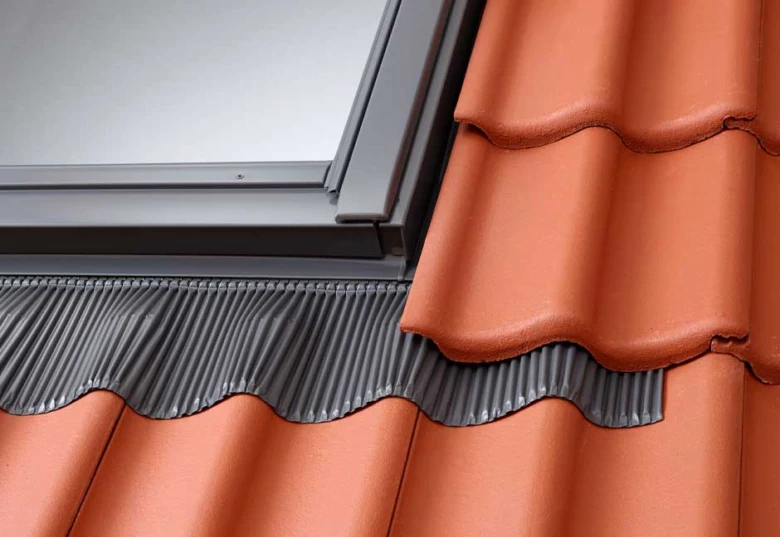 Detailní pohled na montáž šedého střešního lemování pod červenými taškami.