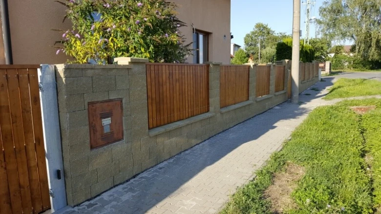 Nový zděný plot s dřevěnými panely po boku chodníku.