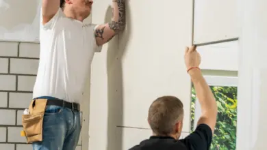 Muži montují bílé panely na stěnu pomocí elektrického nářadí.