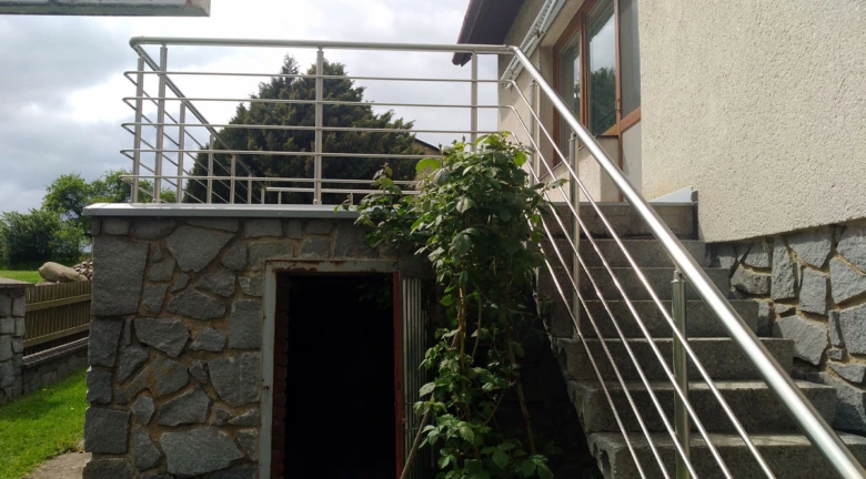 Modern nerezové zábradlí na schodišti vedoucí k domu.