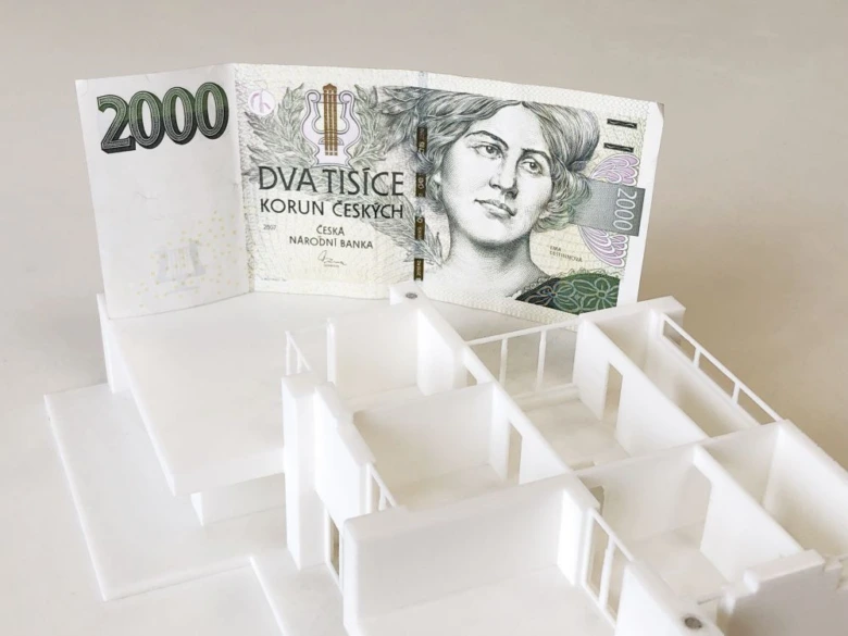 Model domu s českou dvousetkorunovou bankovkou v pozadí.