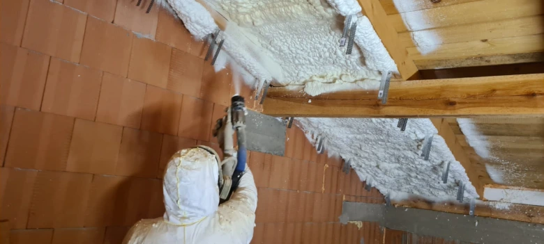 Pracovník aplikuje izolační pěnu mezi trámy střešního krokví.