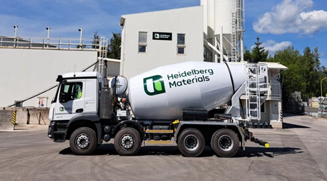 Bílý betonový míchač značky Heidelberg Materials na průmyslovém areálu.