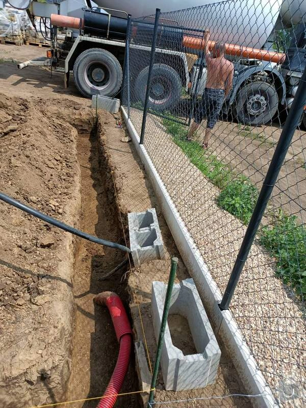 Muž u plotu při instalaci obrubníku s betonovými bloky.