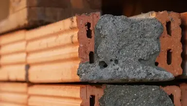 Červené cihly s šedou maltou mezi nimi na zdivu.