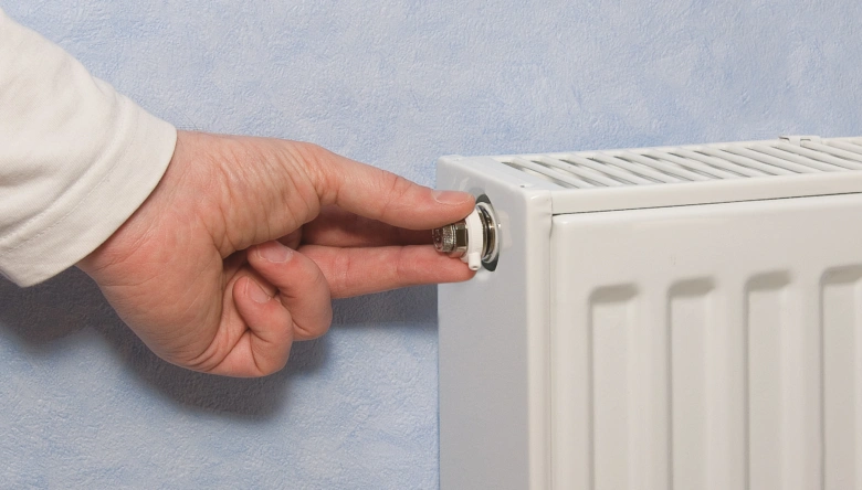 Ruka nastavuje ventilátor na radiátoru u zdi.