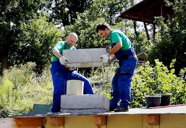 Dva muži staví základ komínu svépomocí venku.