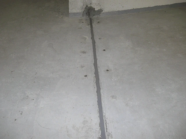 Utěsněná stavební spára na betonové podlaze tmavým těsnicím materiálem.